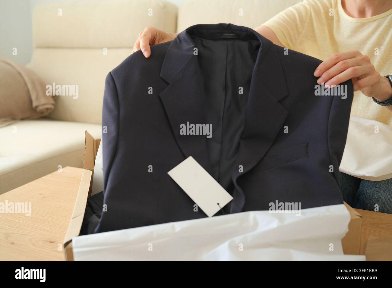 Femme tenant une nouvelle veste sombre sortie d'une boîte d'expédition. Concept d'achat de vêtements en ligne dans l'intérieur de la maison. Femme d'âge moyen déballant le paquet avec Banque D'Images