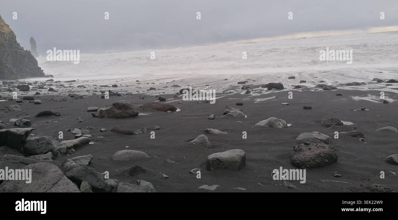 De puissantes vagues s'écrasent sur les sables volcaniques noirs de la plage de Reynisfjara près de Vík í Mýrdal, en Islande, avec l'emblématique cheminée de Reynisdrangar qui s'élève Banque D'Images