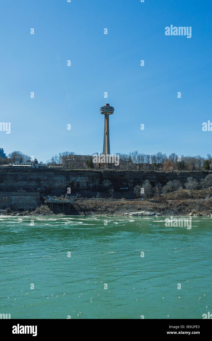 Les gens visitent les chutes du Niagara pour profiter de la vue sur l'eau et les falaises. Skylon Tower se dresse au-dessus du paysage. La rivière scintille sous le soleil, Banque D'Images