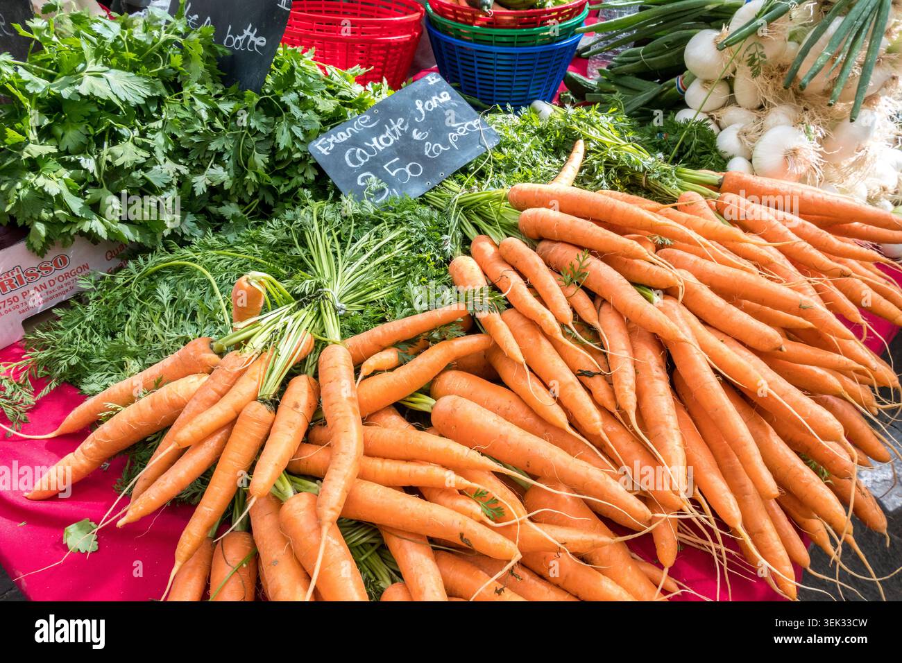 Des grappes fraîches de carottes oranges aux sommets verts sont exposées aux côtés du persil et des oignons verts sur un étal de marché français en plein air avec un panneau de prix, Uzès Banque D'Images