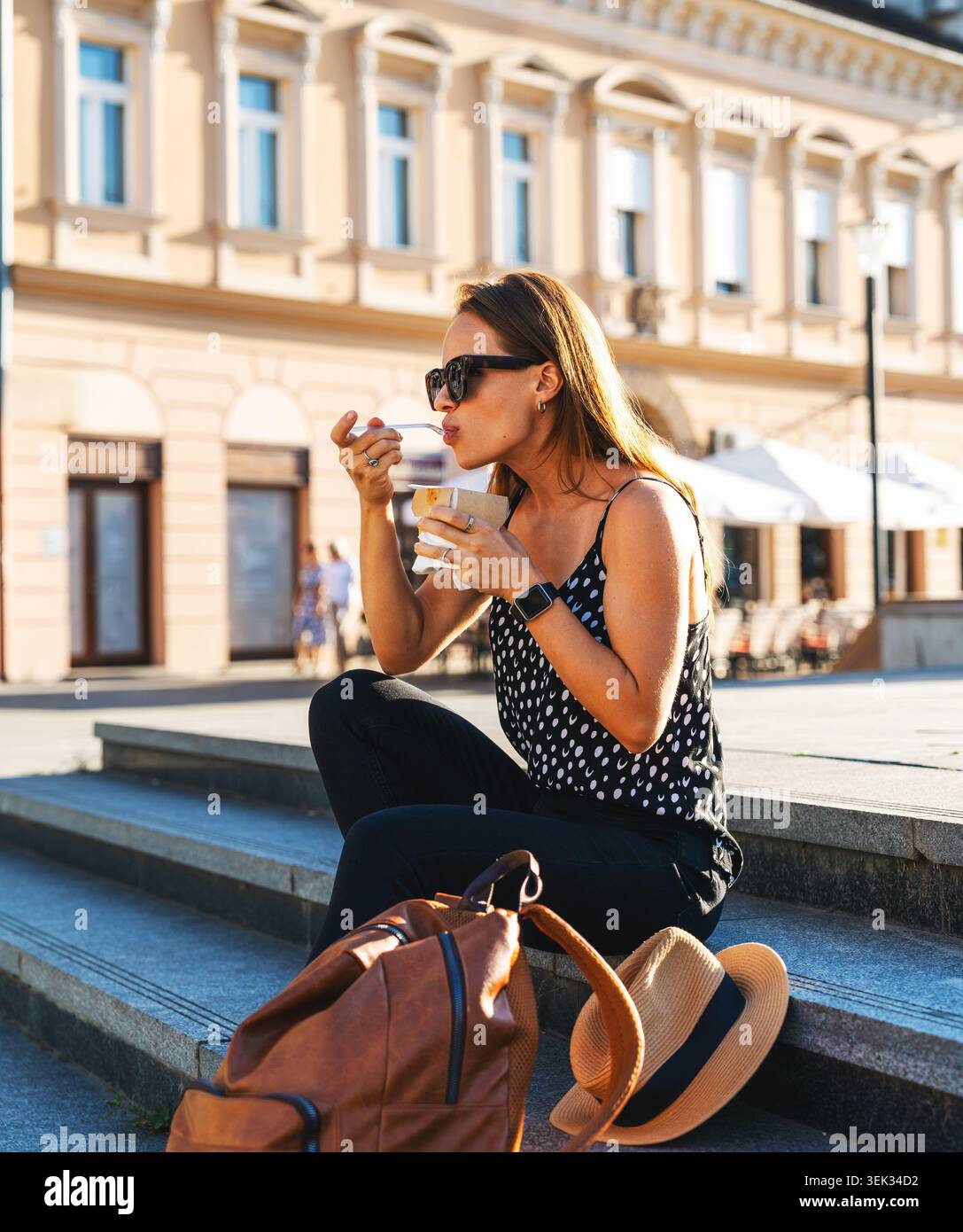 Femme urbaine profitant de son repas à emporter tout en étant assise sur les marches de la rue. Banque D'Images