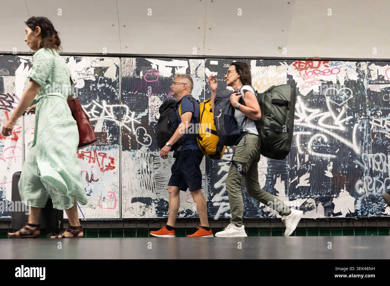 Voyageurs passant devant un mur couvert de graffitis dans le métro de Paris. Banque D'Images