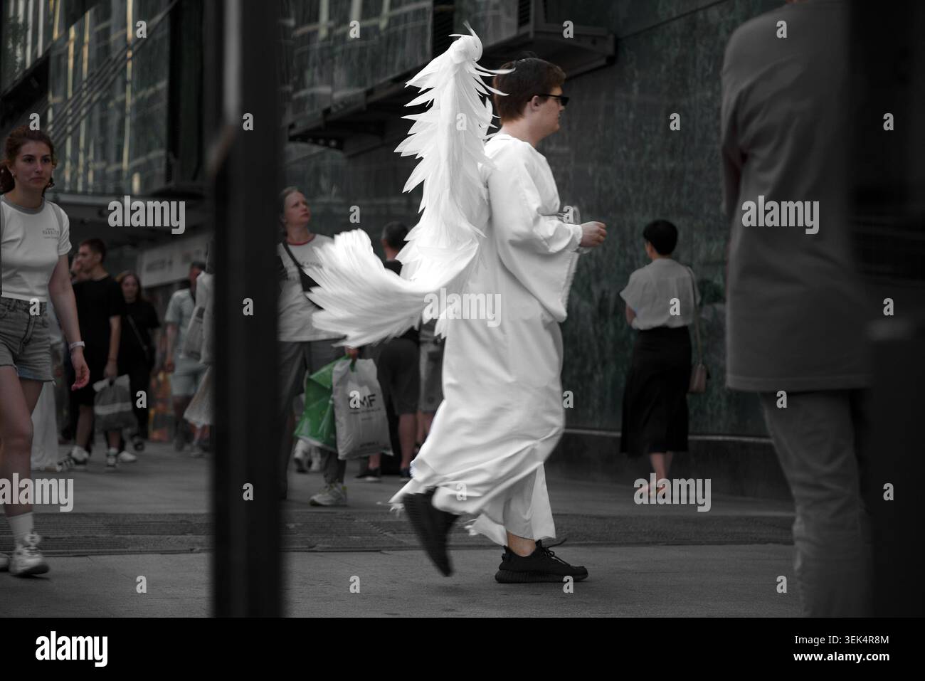 Un homme vêtu d'un costume d'ange blanc avec de grandes ailes à plumes marchant dans une rue animée de la ville Banque D'Images