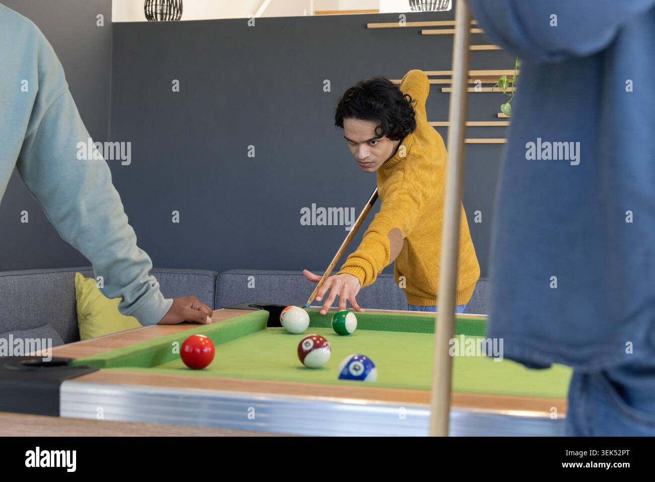 Homme asiatique portant un chandail moutarde et amis penchés sur une table de billard verte dans le salon, CUE de visée Banque D'Images