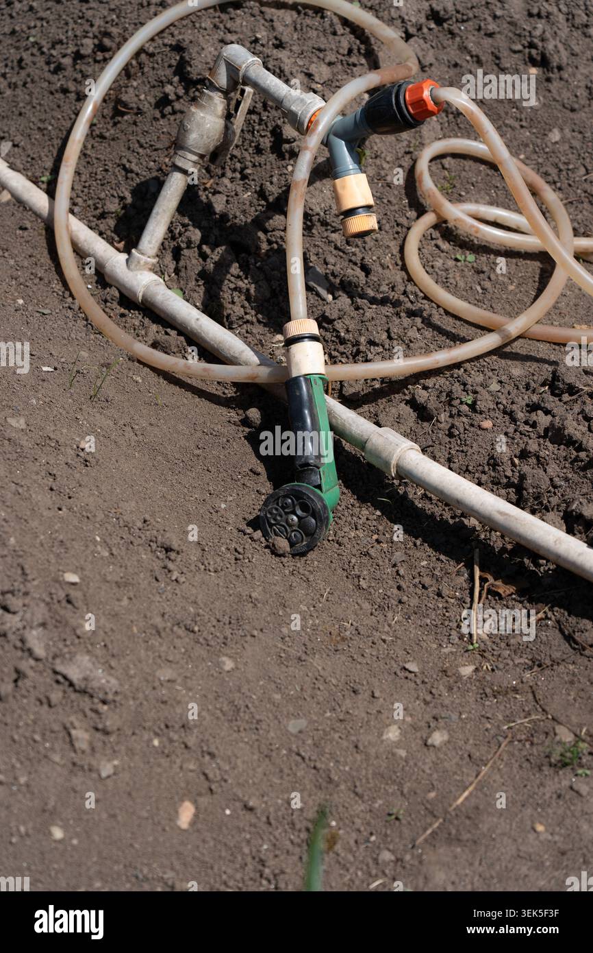 Vue rapprochée de l'équipement d'irrigation sur sol labouré, avec flexibles et connecteurs pour une distribution efficace de l'eau dans les environnements agricoles Banque D'Images