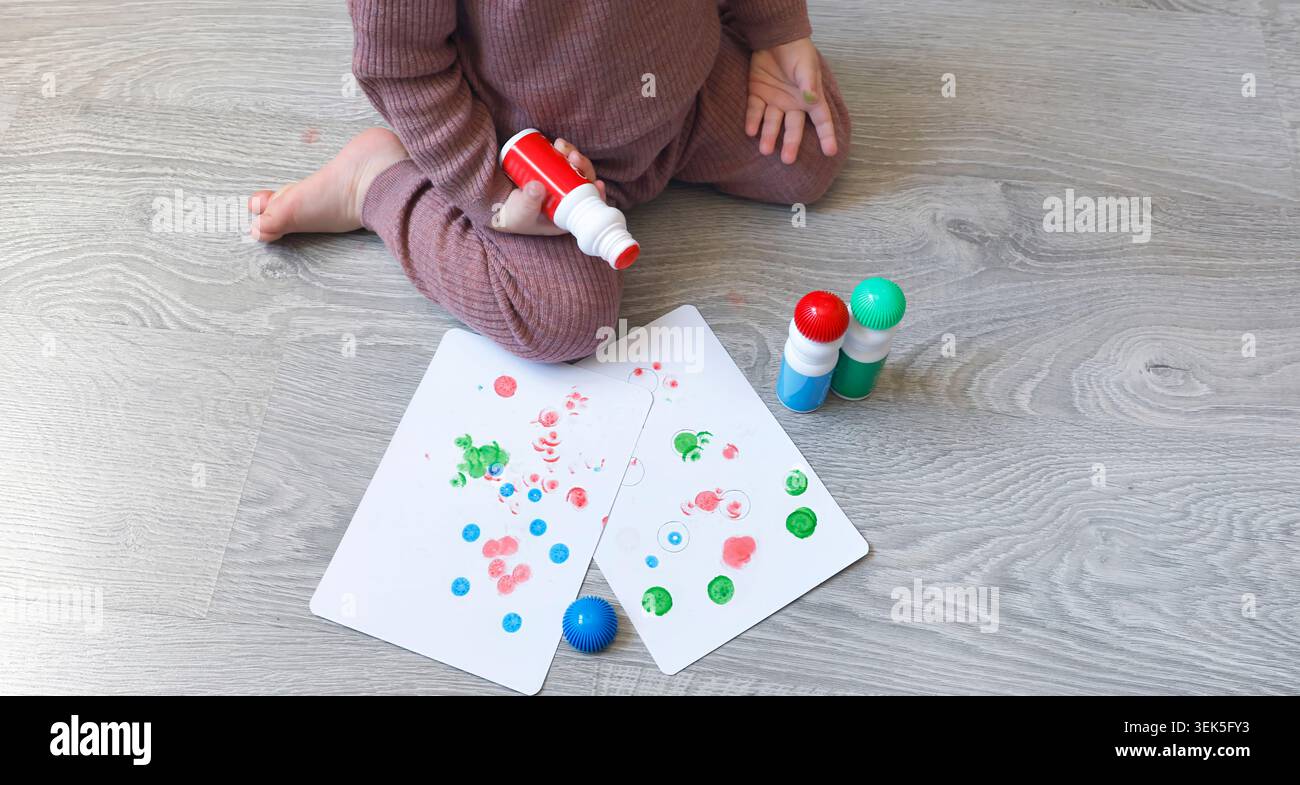 Enfant assis sur le sol tenant un marqueur rouge regardant vers le bas et faisant un choix. Activité éducative créative pour la pensée et le développement de l'enfant à Banque D'Images