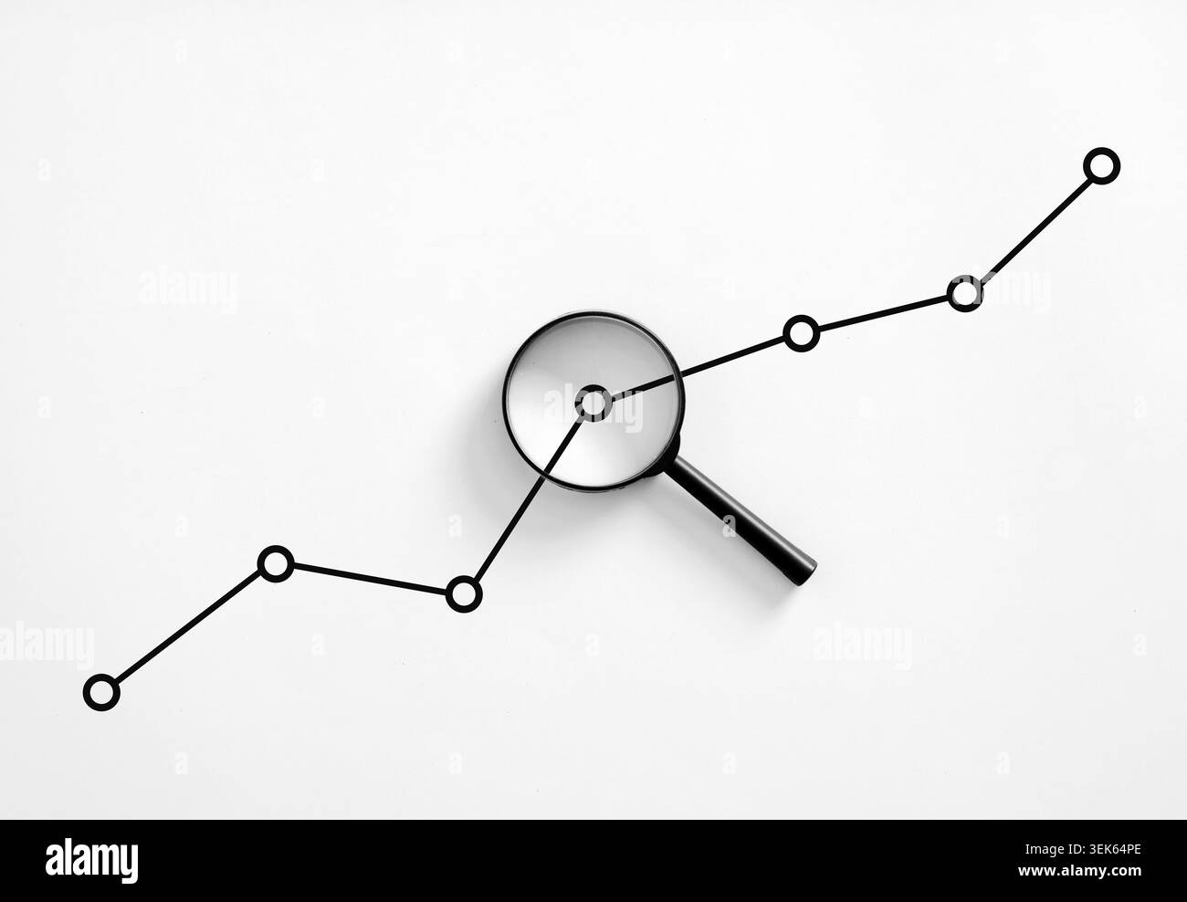 Loupe se concentrant sur un graphique linéaire de tendance à la hausse, symbolisant l'analyse détaillée, l'étude de marché et la planification stratégique de croissance Banque D'Images