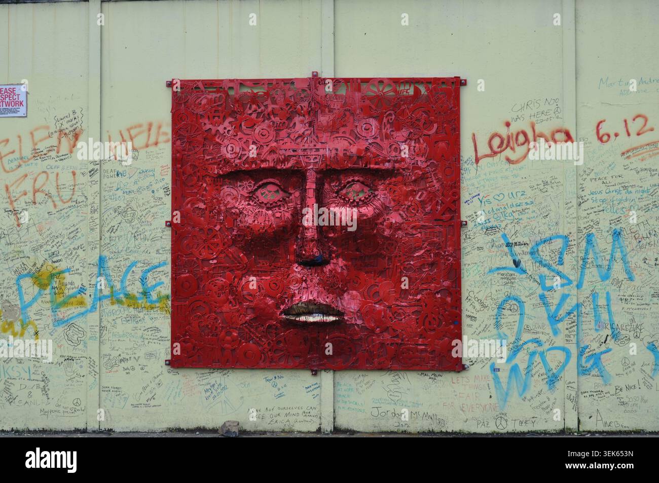 Sculpture carrée à visage métallique rouge montée sur un mur public extérieur recouverte de signatures manuscrites et de graffitis Banque D'Images