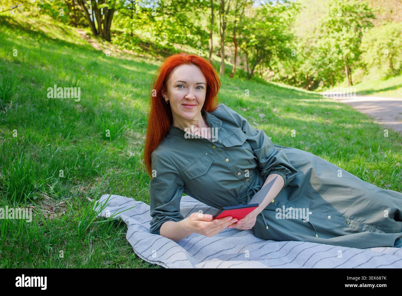 Femme souriante chevelue mi-grimpante lisant ebook dans le parc d'été vert Banque D'Images