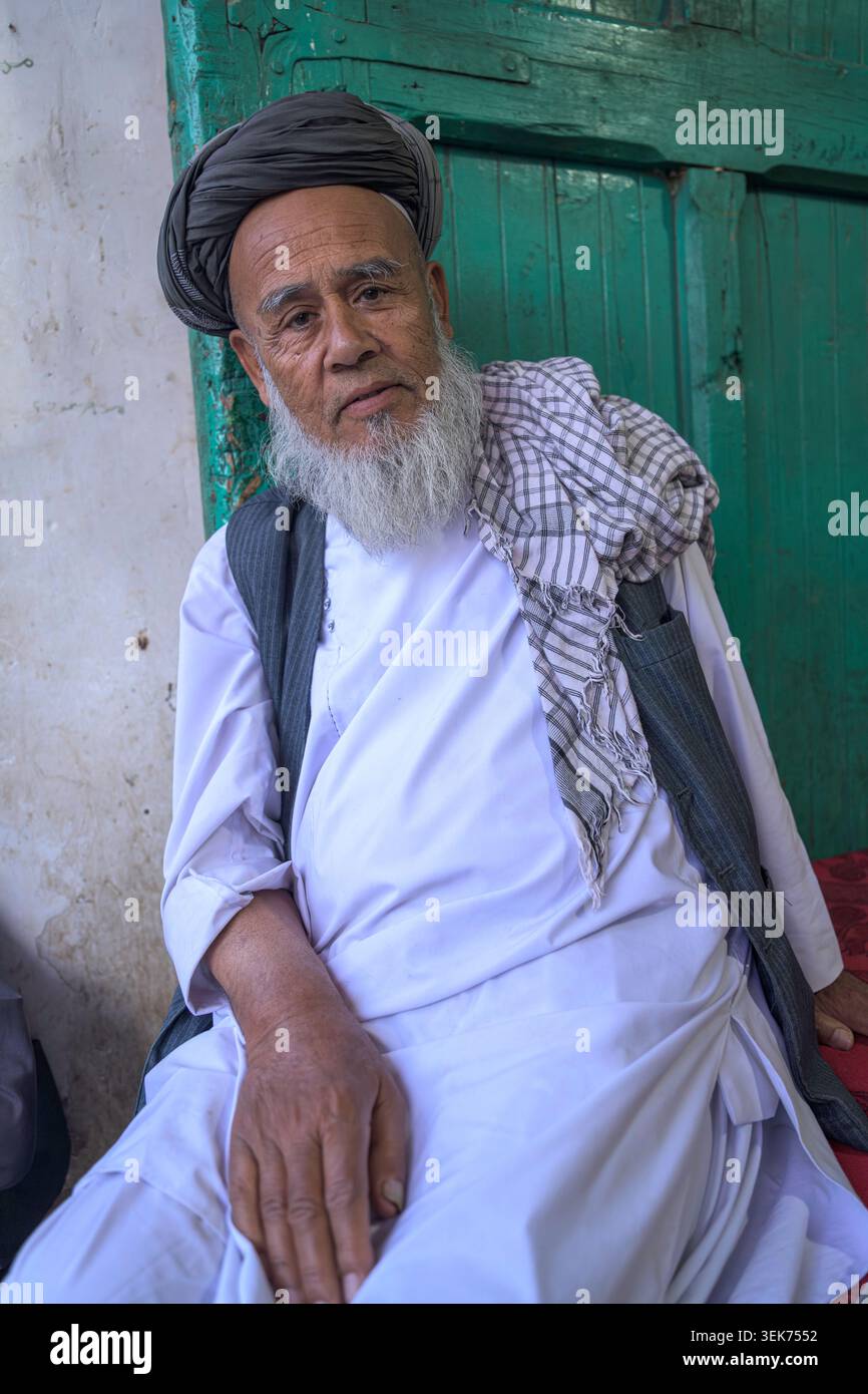 Homme aîné afghan avec une longue barbe blanche assis, regardant attentivement la caméra. Banque D'Images