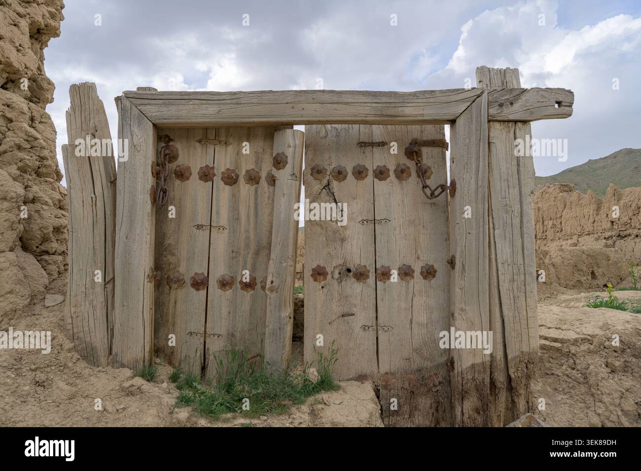 Anciennes portes doubles en bois debout dans un mur de briques de boue en ruine, montrant l'architecture traditionnelle Banque D'Images