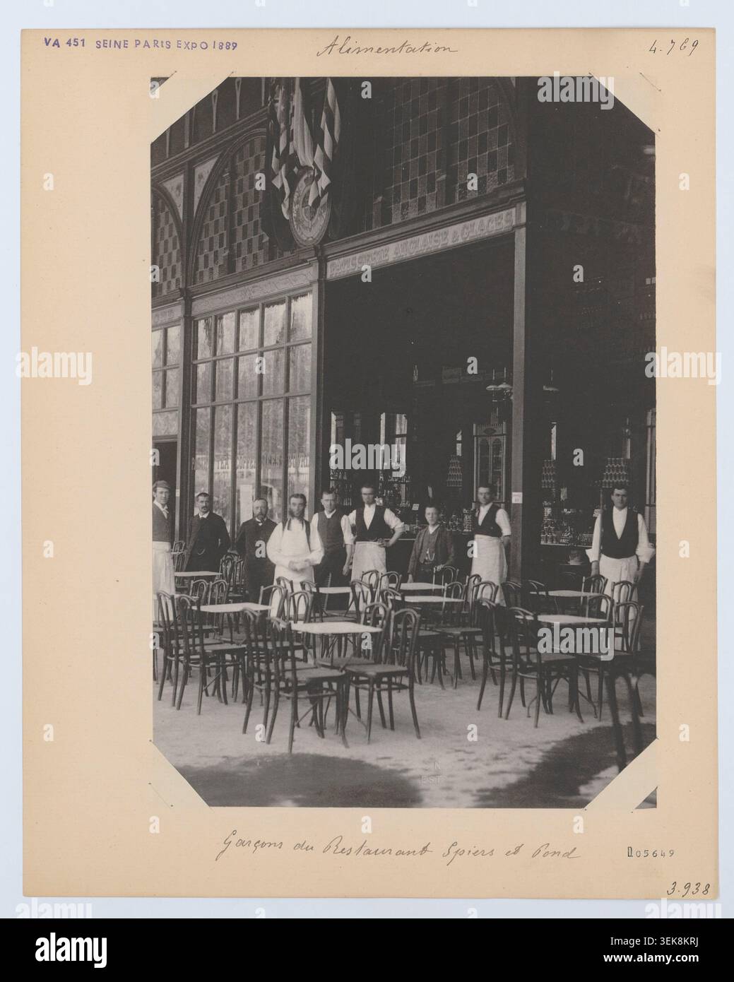 Des serveurs se trouvent parmi les cafés temporaires et les structures d’exposition du champ-de-mars pendant l’exposition internationale de Paris. La photographie montre les travailleurs de l'hôtellerie, les espaces commerciaux de rafraîchissement et les groupes de personnes dans le parc d'exposition. Banque D'Images