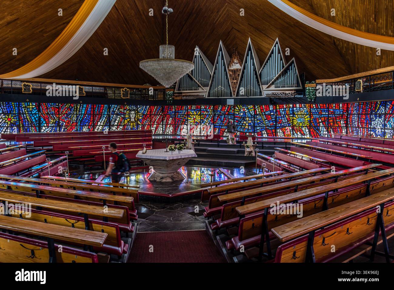 L'intérieur de l'église St Laurentius à Buchbach : un vitrail circulaire encadre la nef circulaire ; l'autel se dresse au centre, tandis que les tuyaux d'orgue font écho à la forme dentelée du toit. La congrégation et le prêtre se réunissent en cercle autour de l’autel – un concept spatial conforme aux enseignements du Concile Vatican II. Bavière, Allemagne Banque D'Images