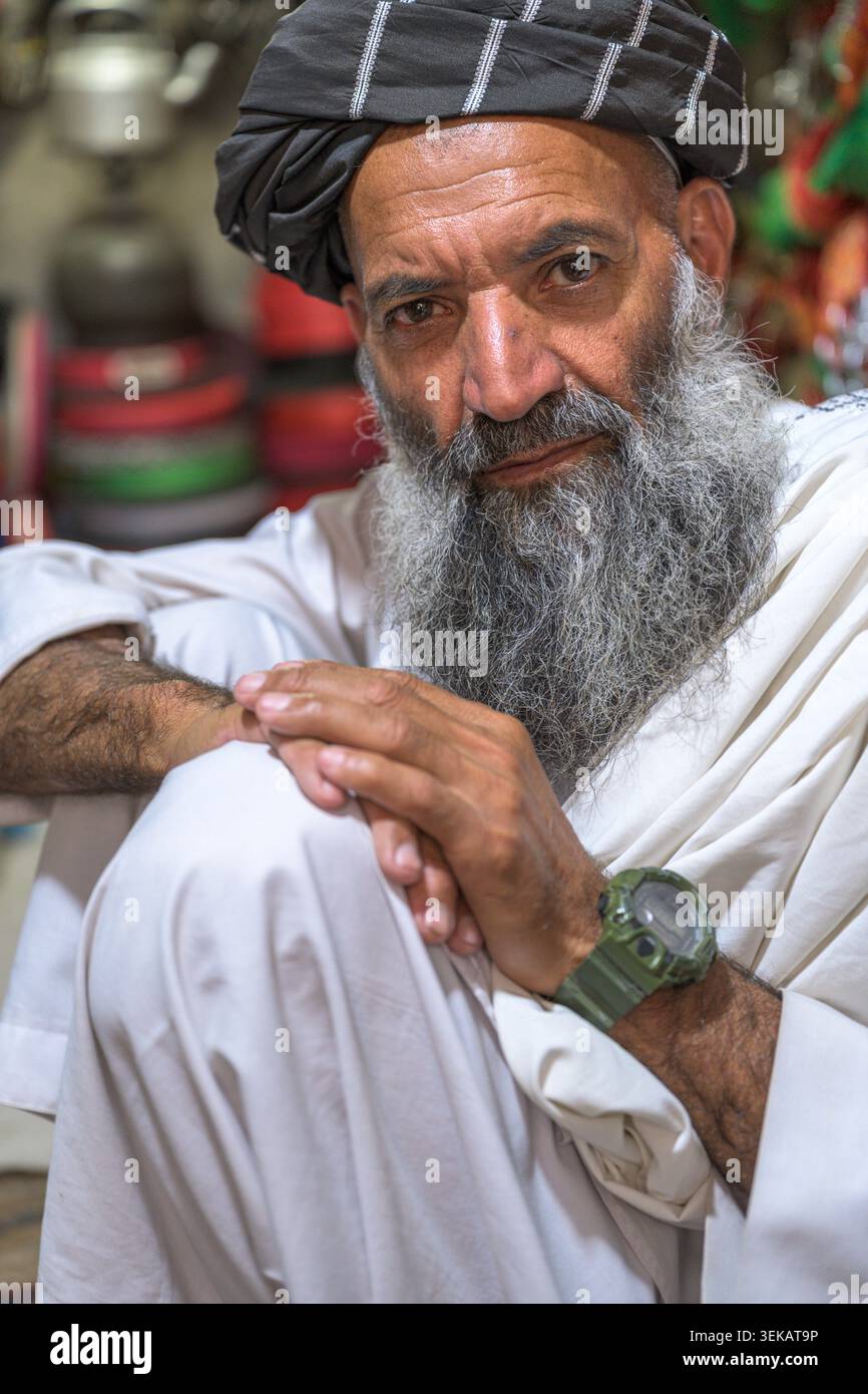Homme afghan avec une longue barbe et turban, portant des vêtements traditionnels. Il est assis, les mains serrées, regardant vers la caméra. Banque D'Images