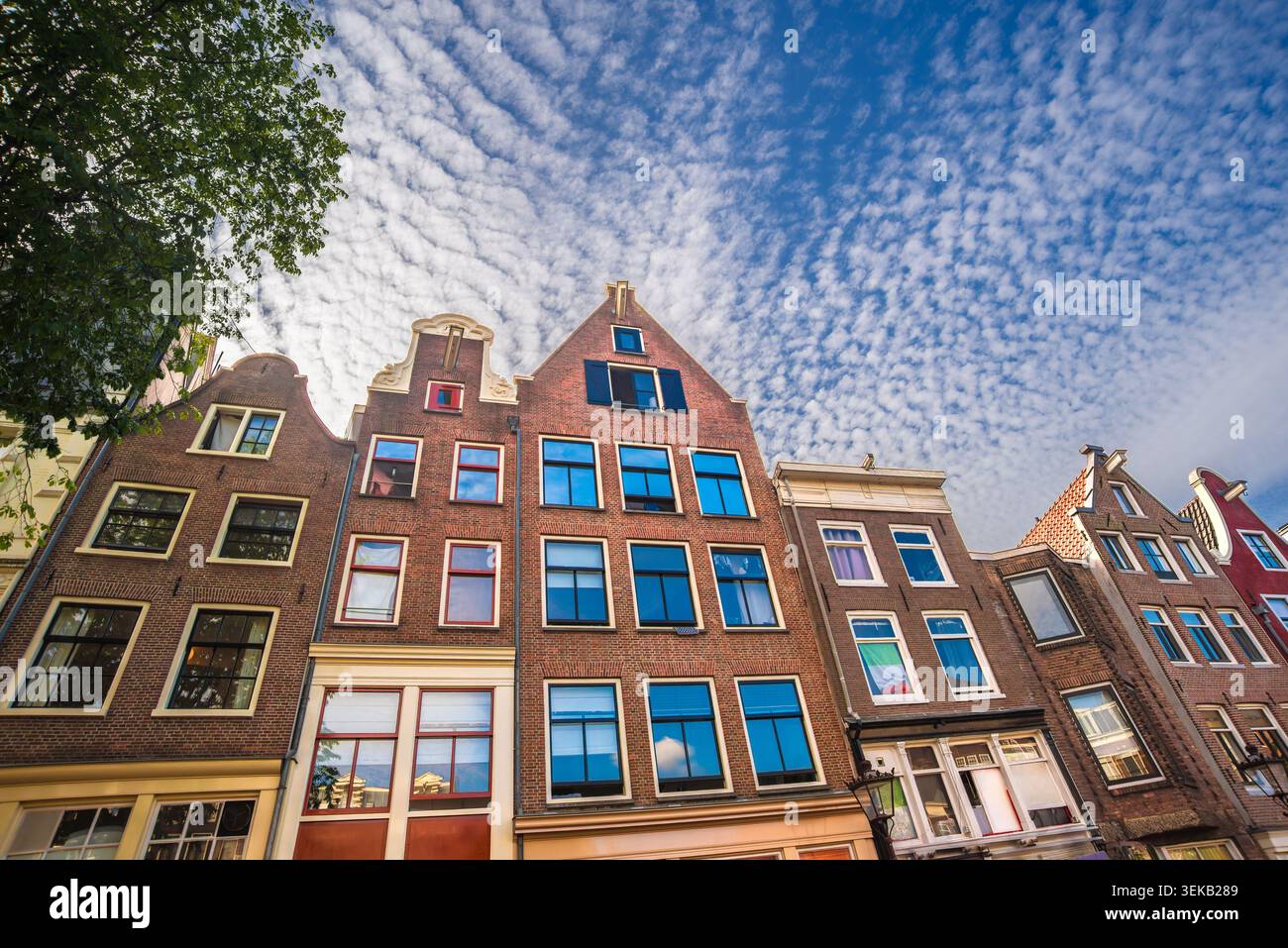 Vue en bas angle des maisons de canal hollandaises traditionnelles avec façades historiques en briques sous un ciel bleu rempli de nuages texturés à Amsterdam, pays-Bas Banque D'Images