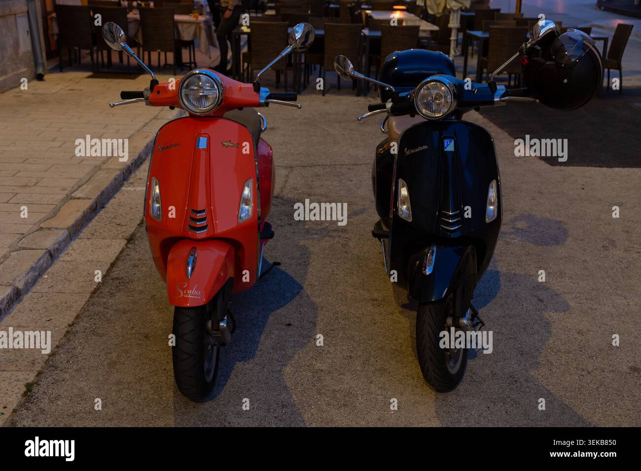 Deux scooters garés, un rouge et un noir, à côté des sièges de café en plein air à Rovinj, Croatie. Banque D'Images