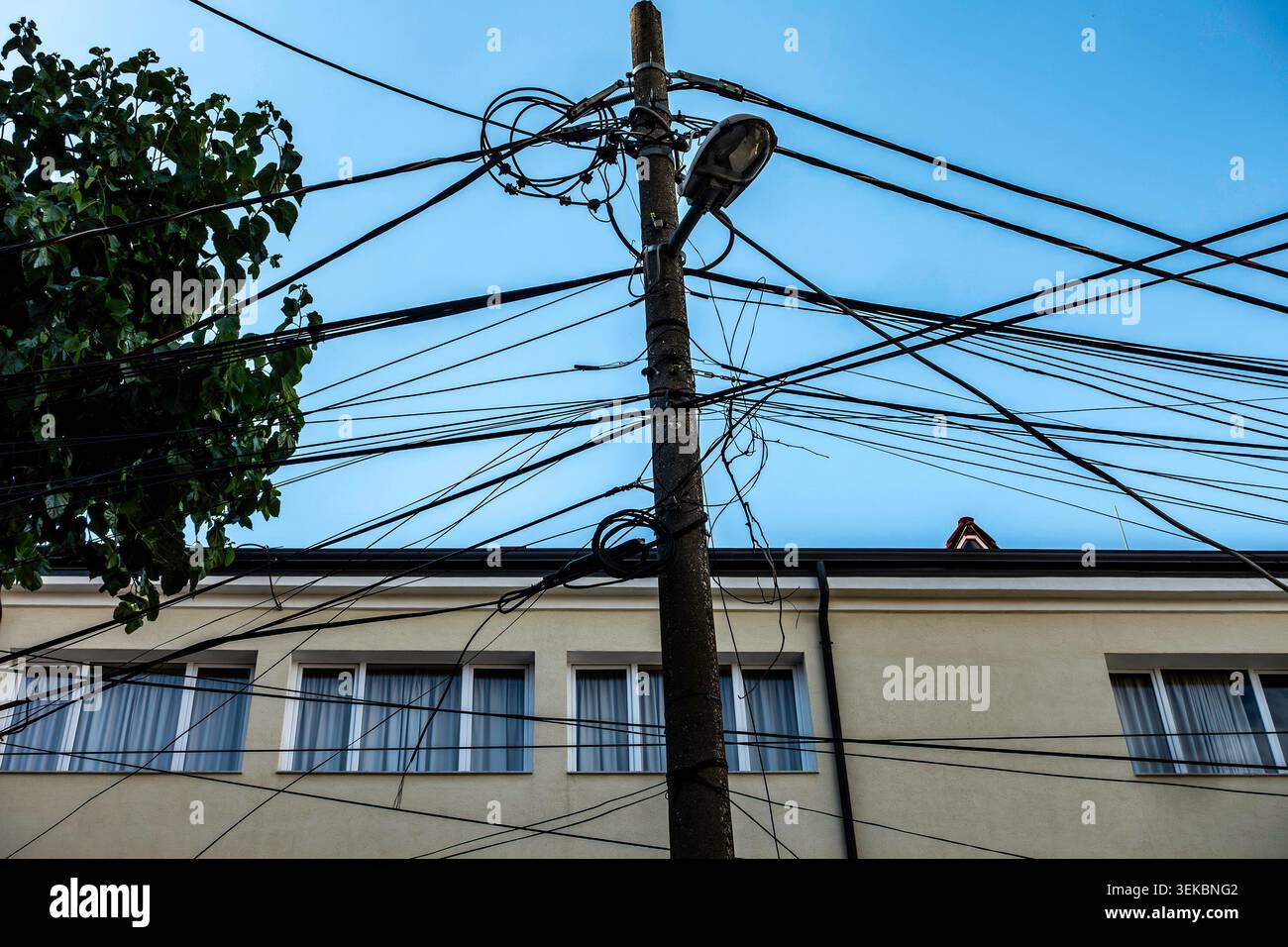 Un poteau électrique à Tirana, en Albanie, enchevêtré avec un désordre dense et chaotique de lignes électriques aériennes et de câbles contre un bâtiment et un ciel bleu. Banque D'Images