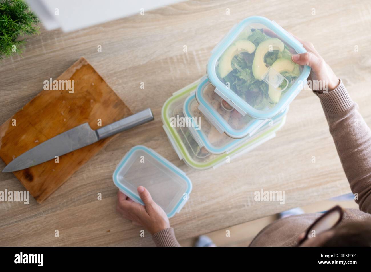 Personne tenant un récipient de stockage des aliments rempli de poulet grillé, de riz et de brocoli tout en préparant des repas sains à la maison. Banque D'Images