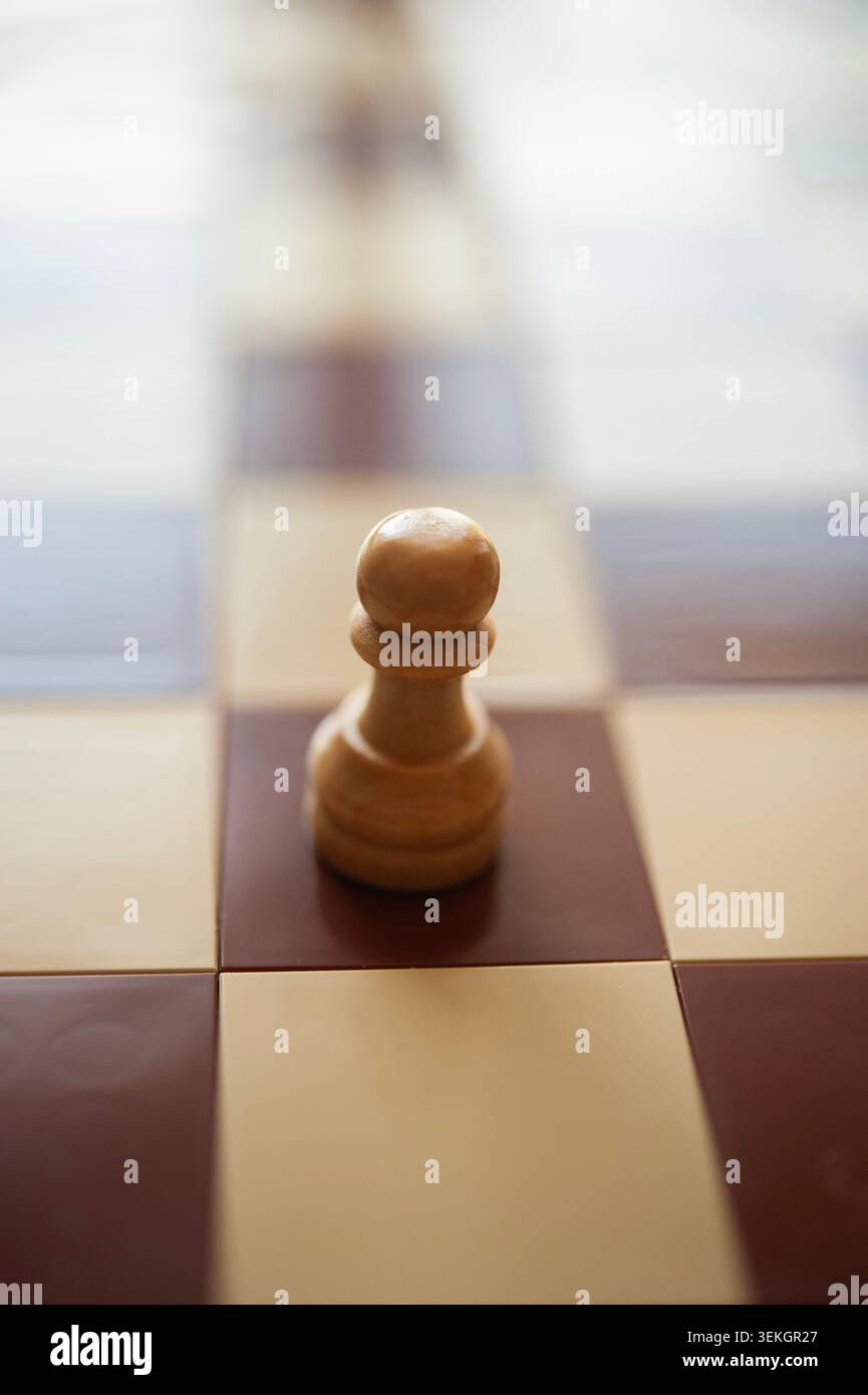 Pion d'échecs en bois seul sur échiquier, lumière chaude et peu profonde, concept de stratégie minimaliste Banque D'Images