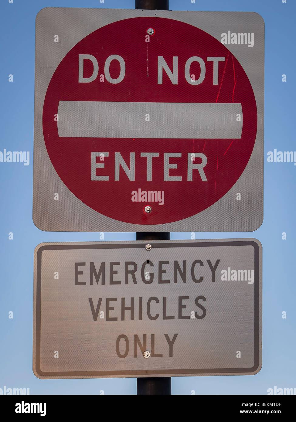 Panneau routier « ne pas entrer » rouge américain monté au-dessus d'une plaque de restriction véhicules d'urgence seulement sur un poteau métallique contre un ciel bleu clair Banque D'Images