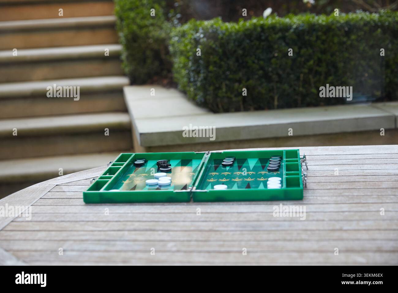 Plateau de backgammon vert installé sur une table de jardin en bois pour un jeu en plein air dans un cadre de patio privé. Banque D'Images