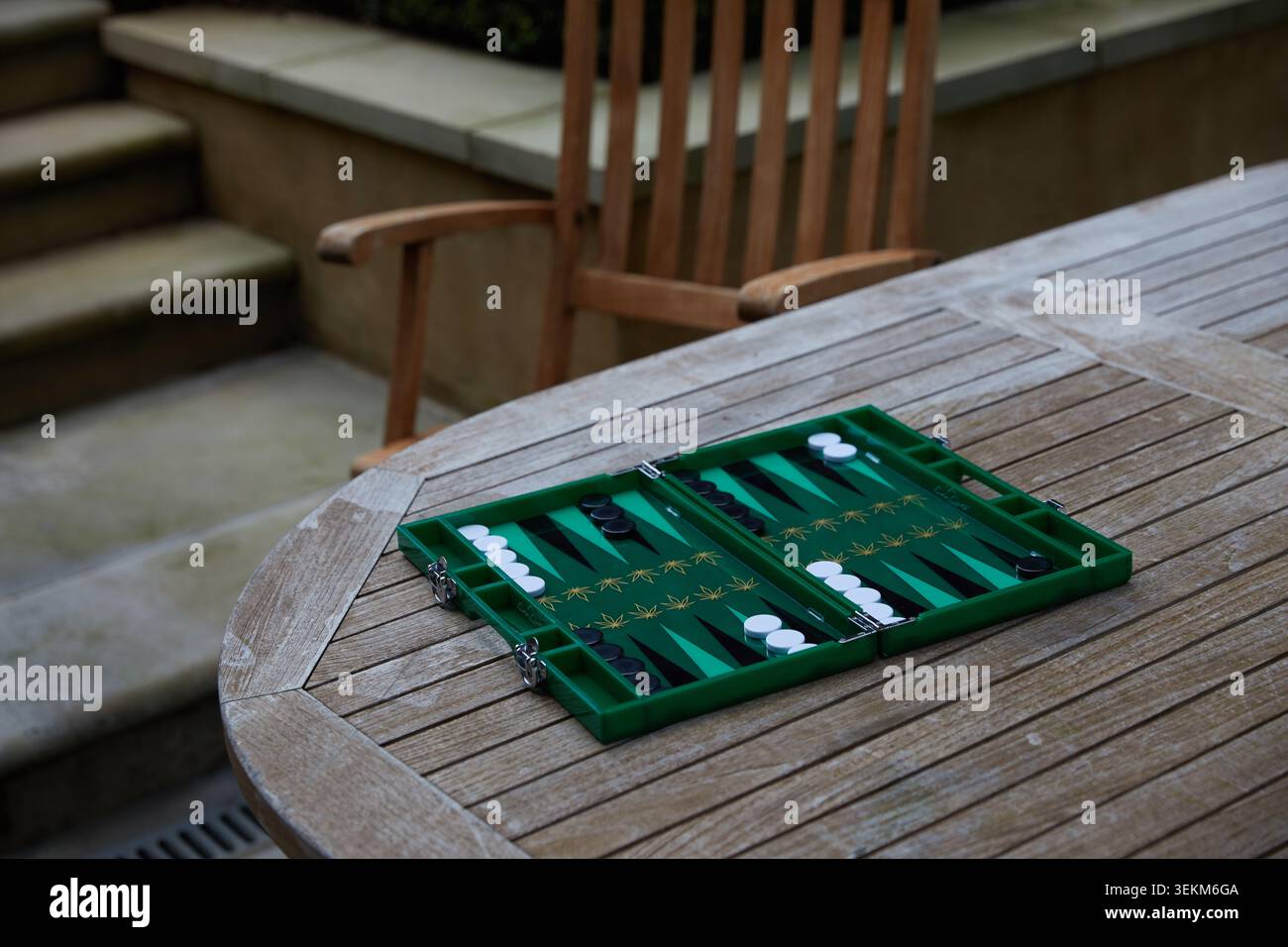 Plateau de backgammon vert installé sur une table de jardin en bois pour un jeu en plein air dans un cadre de patio privé. Banque D'Images