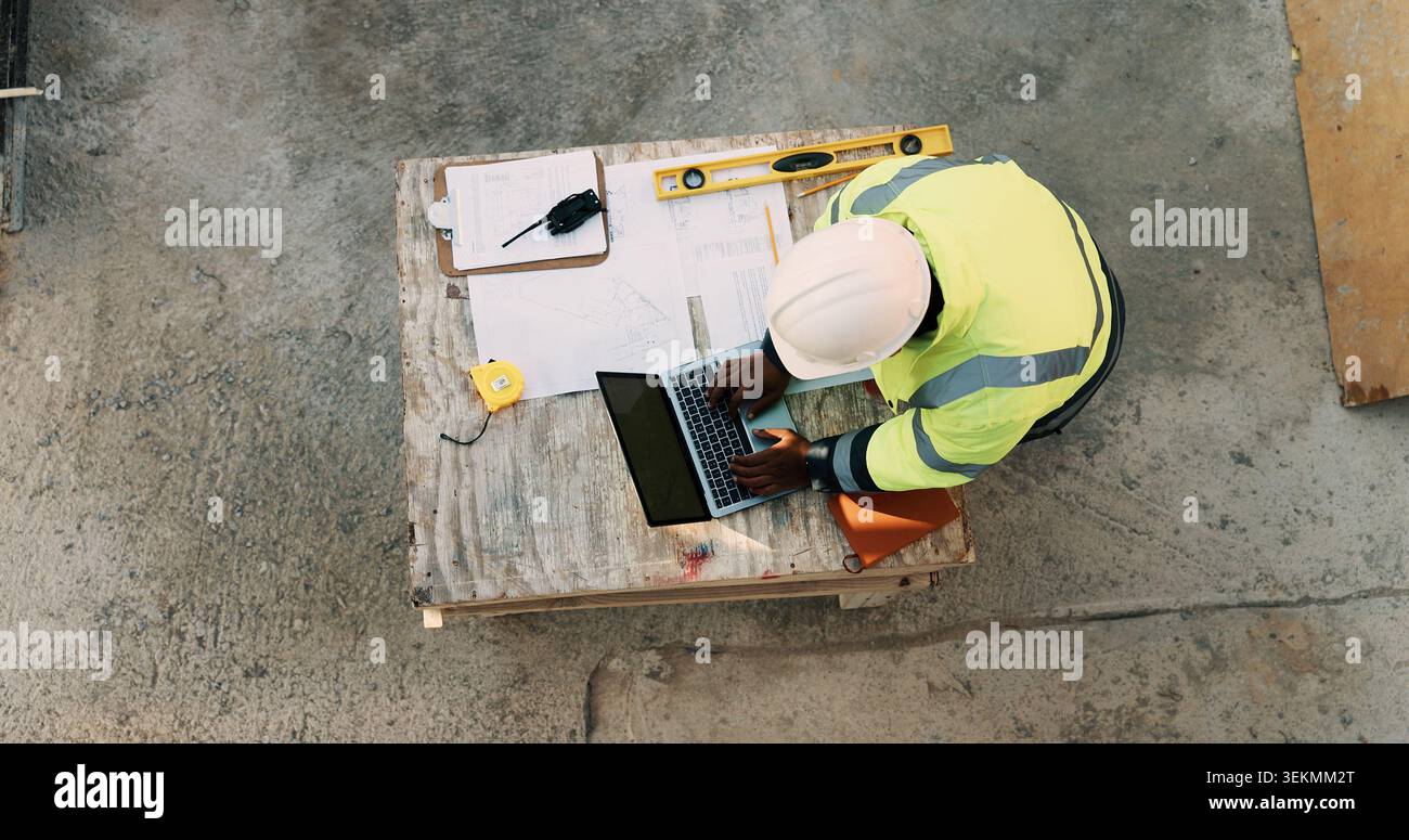 Documents, ordinateur portable et au-dessus de l'homme sur le chantier de construction pour la planification, le permis de construire et la conformité. Architecture, ingénieur et personne sur ordinateur Banque D'Images