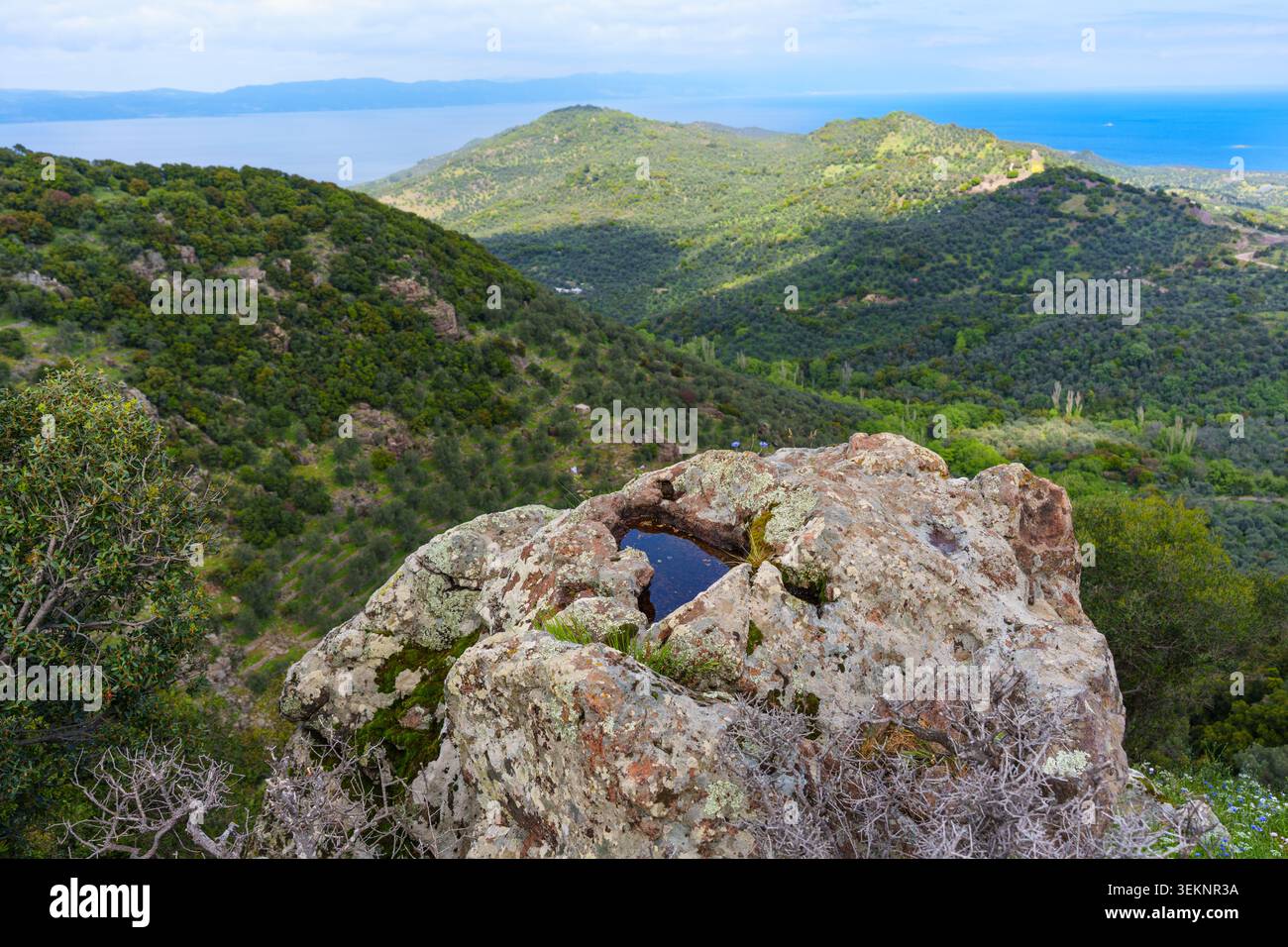 Roche de premier plan accidentée avec un petit bassin d'eau surplombant les vastes collines verdoyantes et l'horizon bleu lointain de la mer Égée près de Kleio vil Banque D'Images