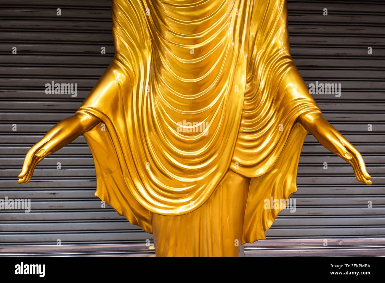 Gros plan détaillé d'une statue dorée de Bouddha, mettant en évidence les mains gracieusement étendues et les plis complexes de la robe monastique, dressée contre Banque D'Images