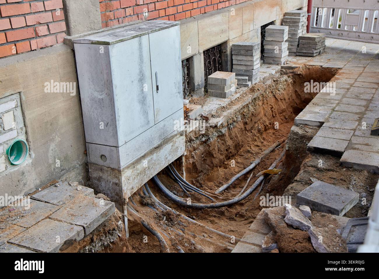 Câbles souterrains exposés dans une tranchée profonde sous une boîte de distribution électrique lors de la construction de rues. Banque D'Images