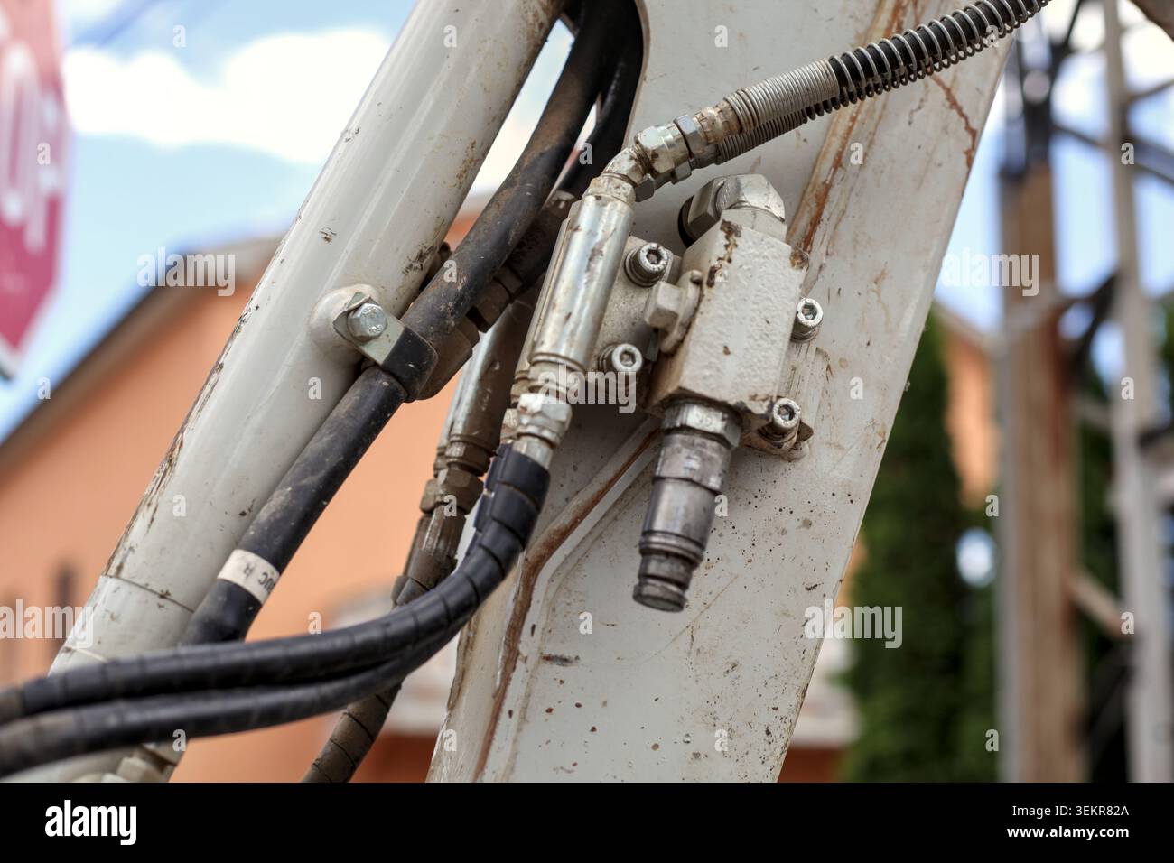 Gros plan montrant des flexibles hydrauliques complexes, des vannes métalliques, des raccords et des conduites de fluide circulant le long d'un bras de pelle blanc sale. Banque D'Images