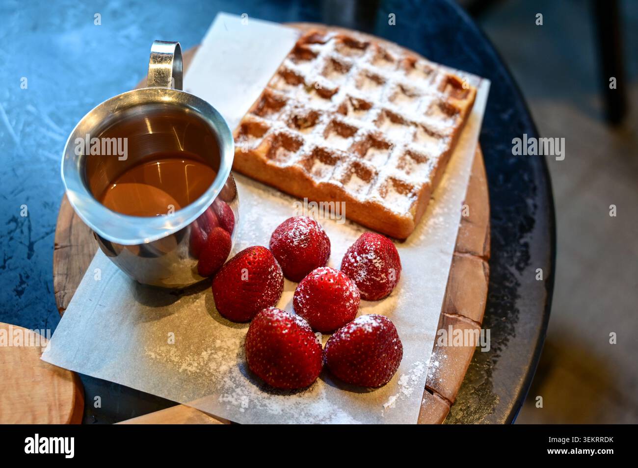 Gros plan d'un pichet à sirop, d'une gaufre en poudre et de fraises fraîches sur une planche de bois, d'un concept de nourriture pour petit déjeuner ou dessert pour les menus et les blogs alimentaires. Banque D'Images