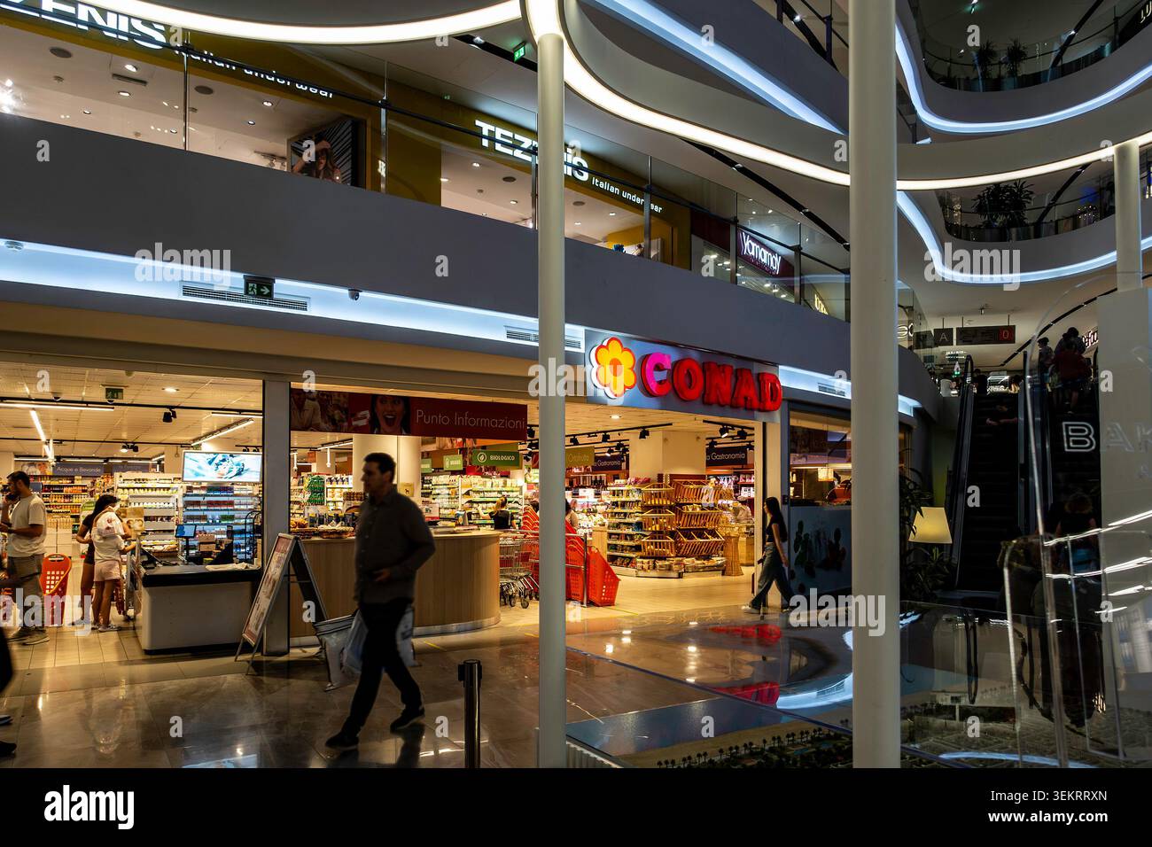 Les acheteurs marchent près d'un supermarché Conad et d'un magasin Tezenis dans l'intérieur à plusieurs niveaux du centre commercial Toptani à Tirana, en Albanie. Banque D'Images
