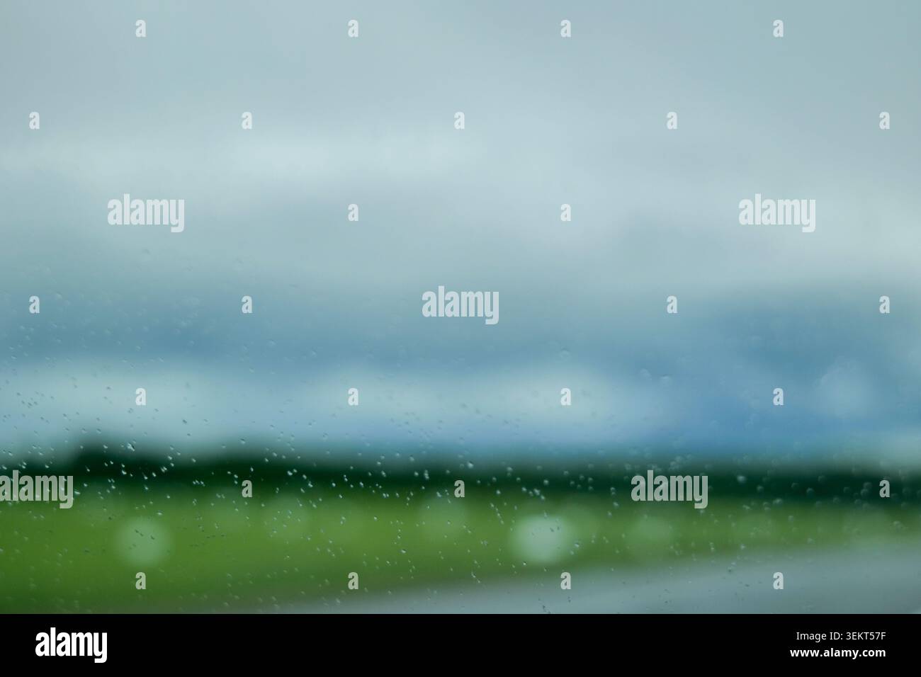 Gouttes de pluie sur une fenêtre de voiture avec champ vert flou et ciel nuageux Banque D'Images
