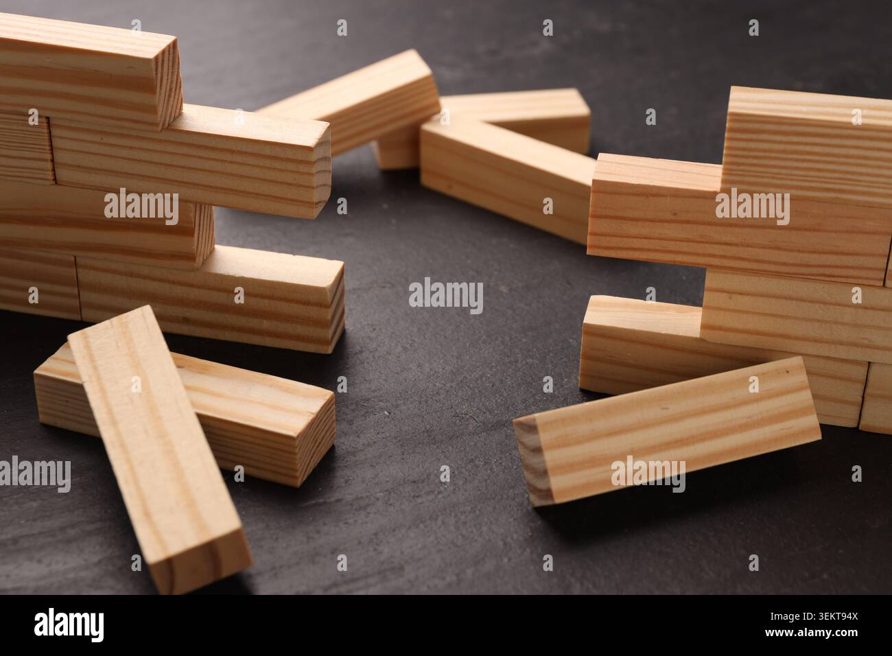 Mur en bois effondré fait de blocs sur la table noire, gros plan. Surmonter les obstacles Banque D'Images