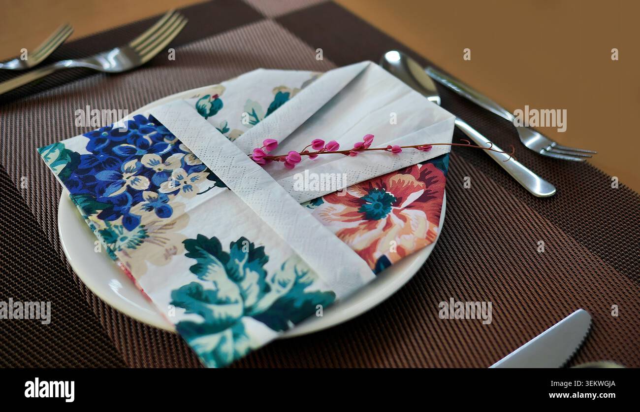 Cadre de table élégant avec une technique unique de pliage de serviette double couche, serviette en papier blanc texturé entrelacé avec serviette en tissu à imprimé floral. Banque D'Images