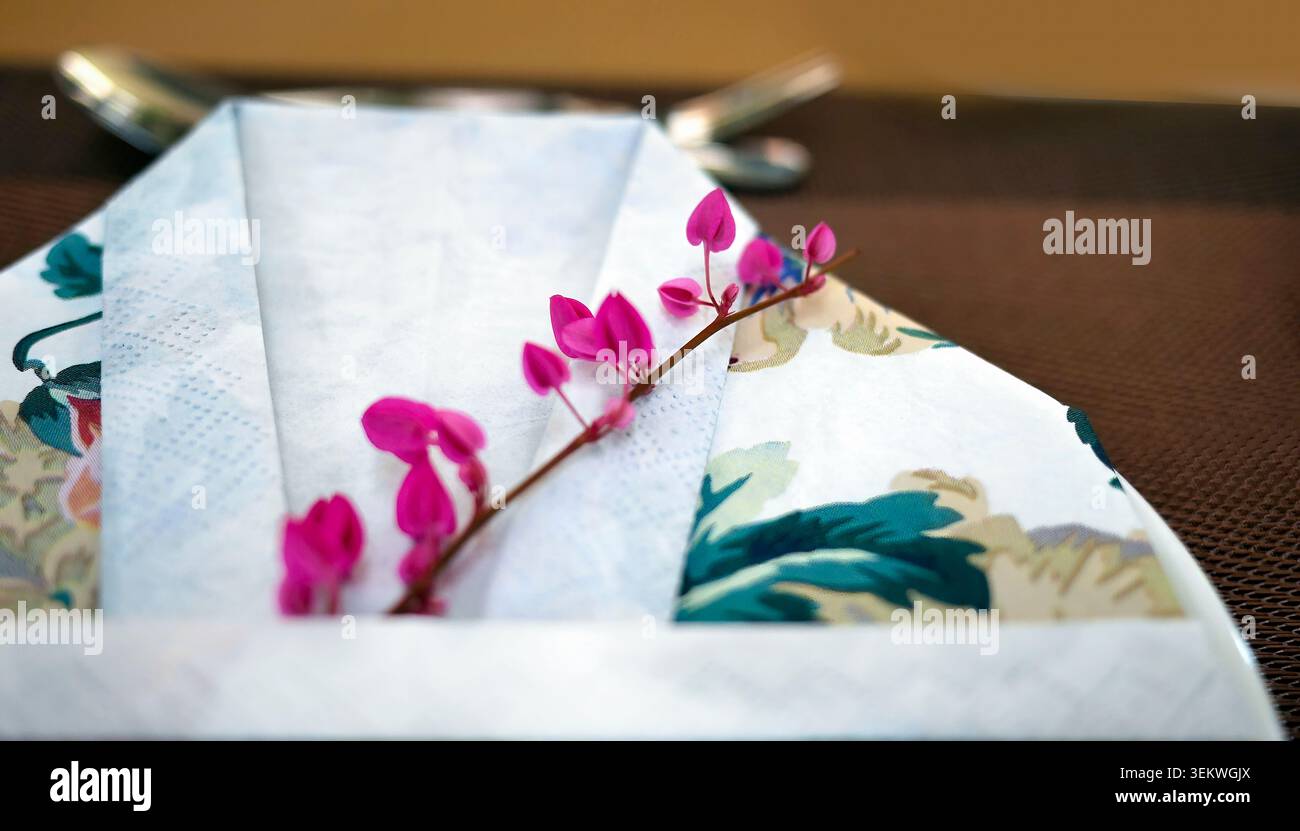 Cadre de table élégant avec une technique unique de pliage de serviette double couche, serviette en papier blanc texturé entrelacé avec serviette en tissu à imprimé floral. Banque D'Images