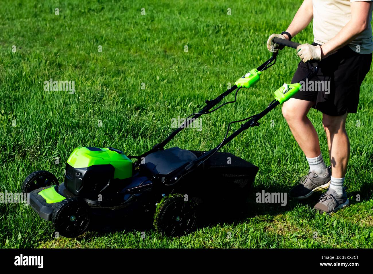Un homme tond l'herbe avec une tondeuse à gazon sans fil Banque D'Images