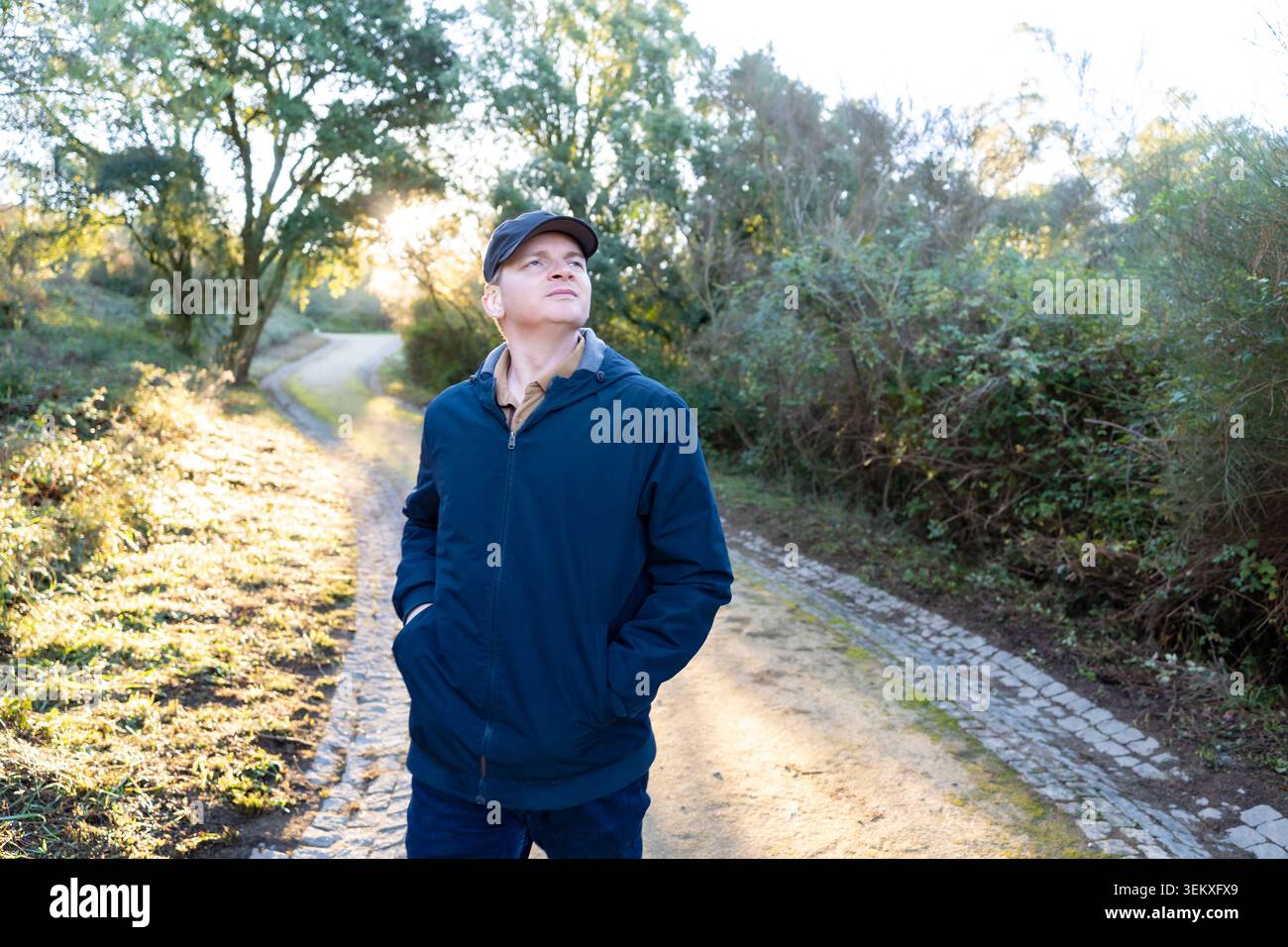 Homme dans une veste bleue et casquette marchant un chemin extérieur, levant les yeux avec une expression contemplative Banque D'Images