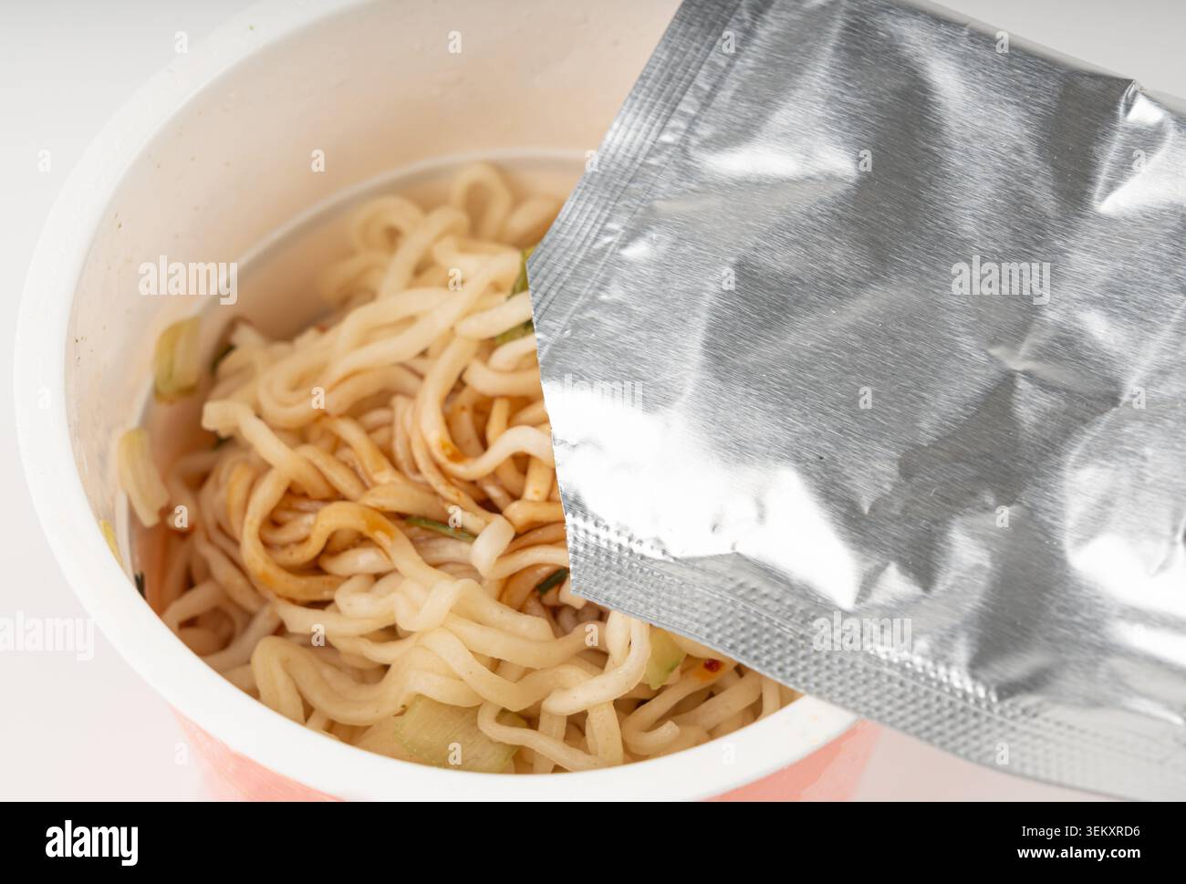 Nouilles instantanées sèches cuisant dans une tasse isolée. ajout d'épices aux spaghettis dans l'eau chaude, pâtes alimentaires rapides dans le récipient, nouilles ramen instantanées ouvertes Banque D'Images