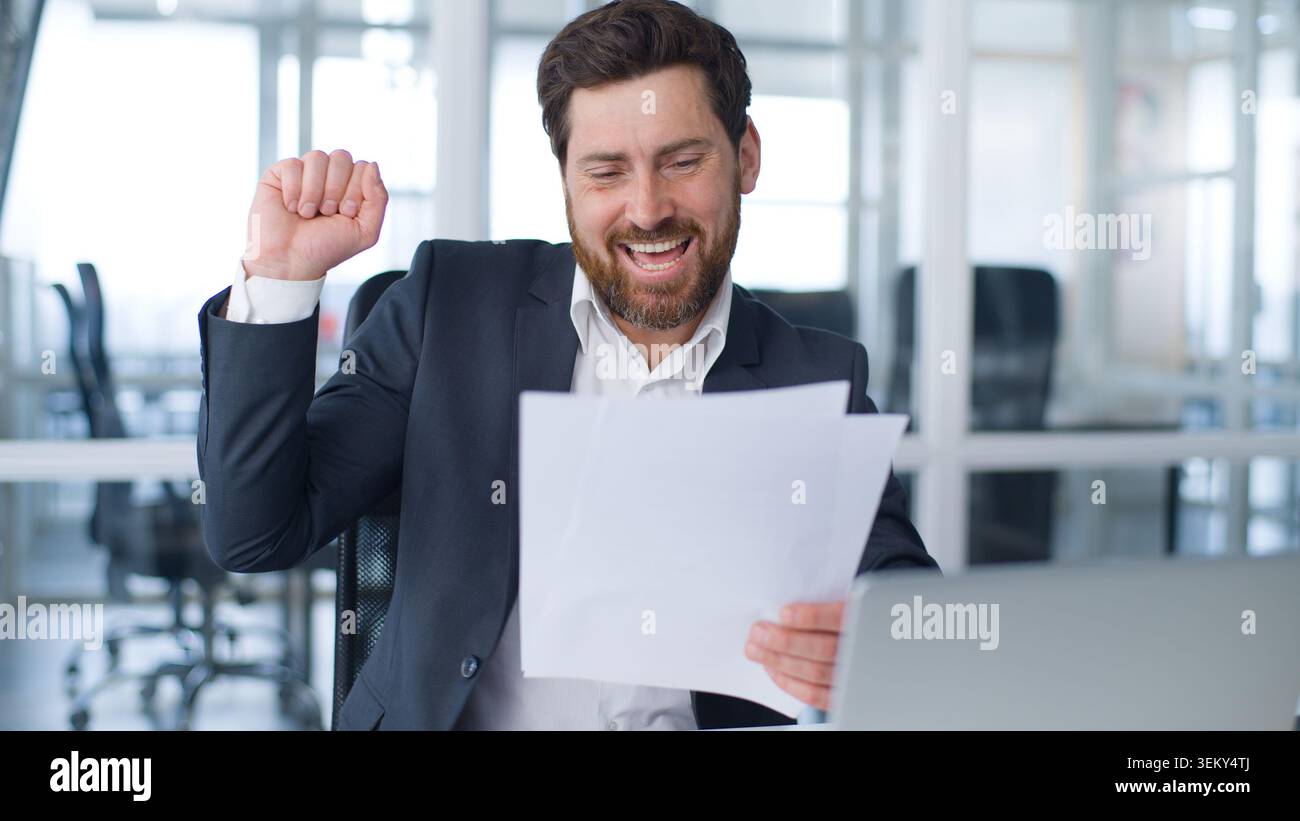 Motivé homme d'affaires caucasien d'âge moyen heureux avec des documents de bons résultats danse réjouissant contrat de conclusion de travail avec de la musique en compagnie Banque D'Images