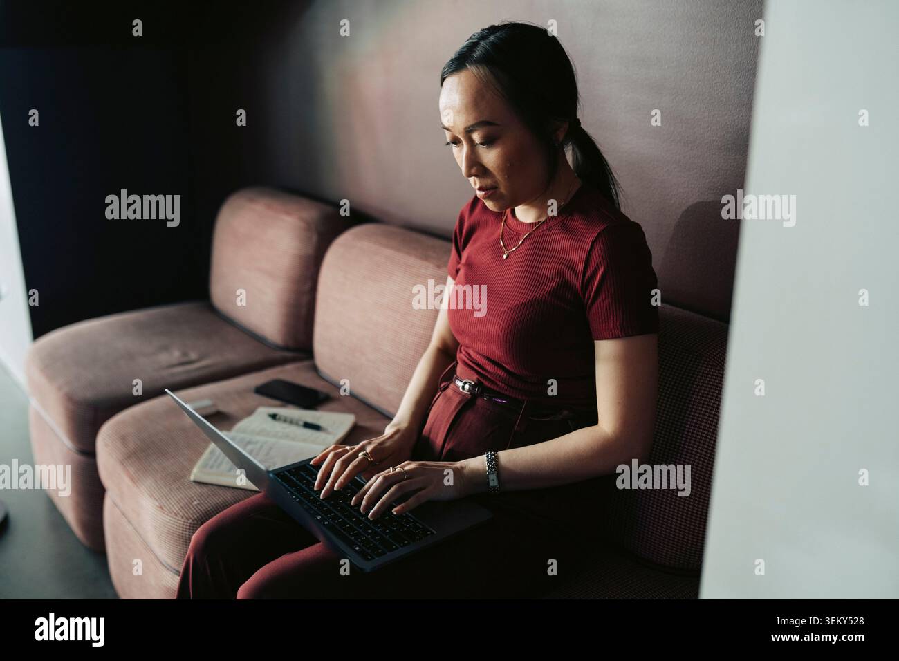 Femme d'affaires travaillant sur ordinateur portable tout en étant assis sur le canapé à l'espace de travail moderne Banque D'Images