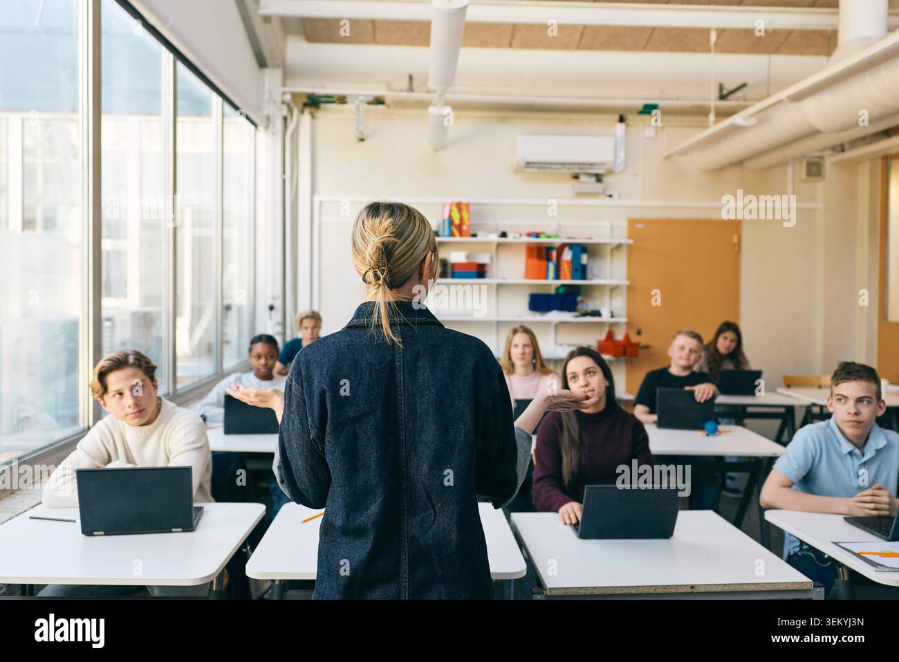 Vue arrière d'une femme professeure enseignant des élèves du premier cycle du secondaire en classe Banque D'Images