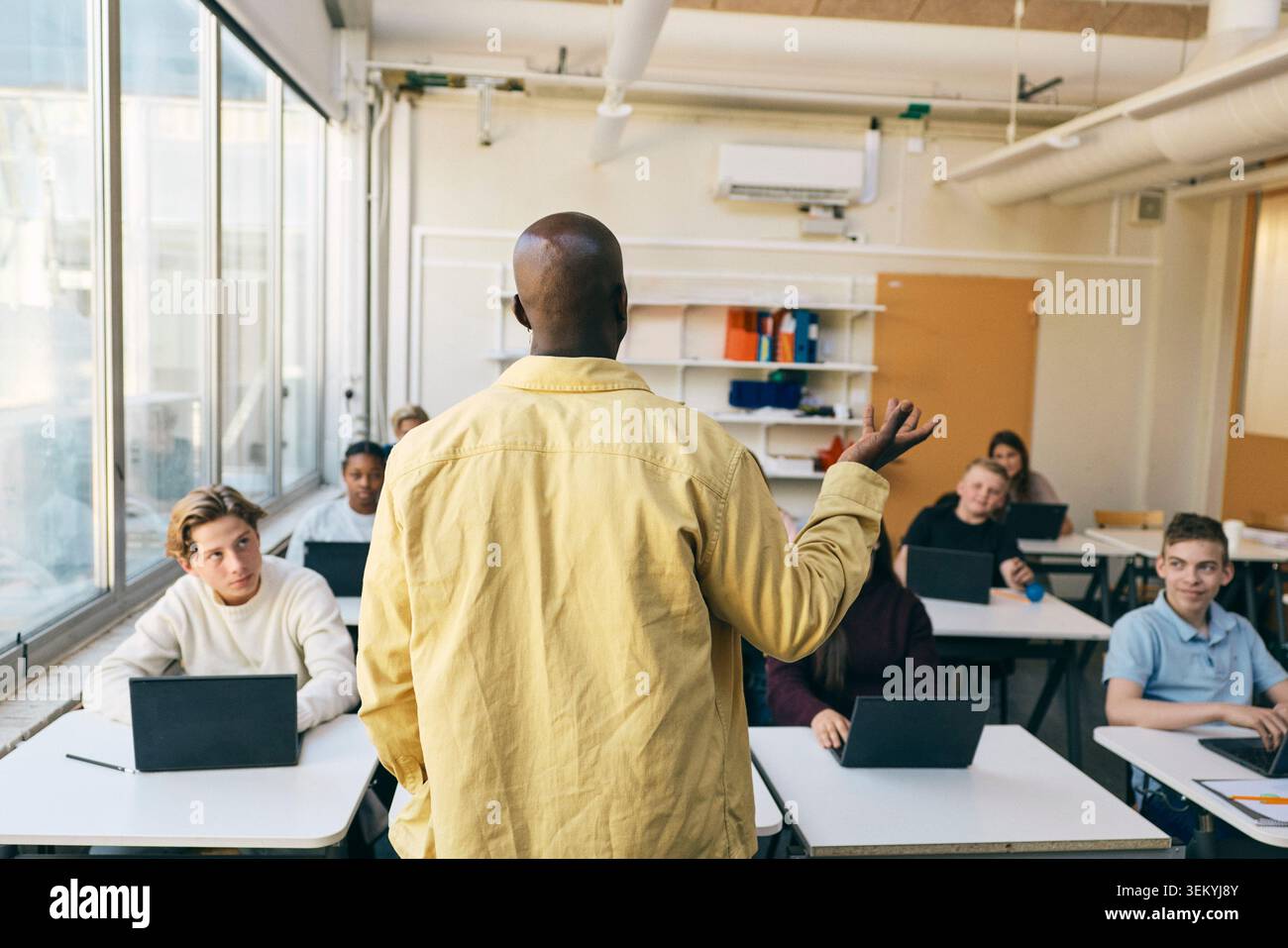 Vue arrière d'un professeur masculin enseignant des élèves en classe au collège Banque D'Images