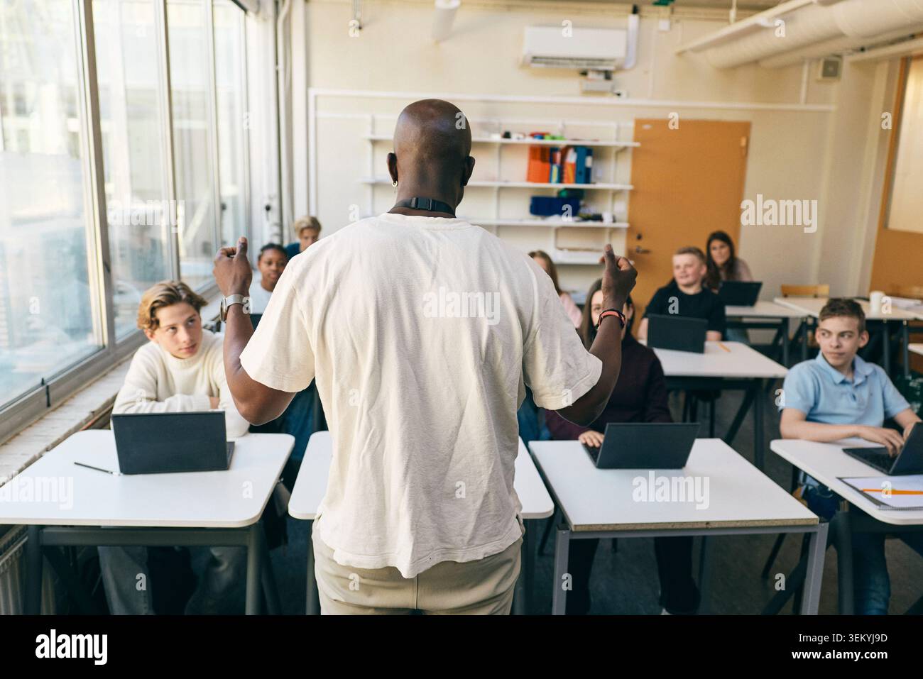 Vue arrière d'un enseignant masculin faisant des gestes avec des élèves du secondaire en classe Banque D'Images