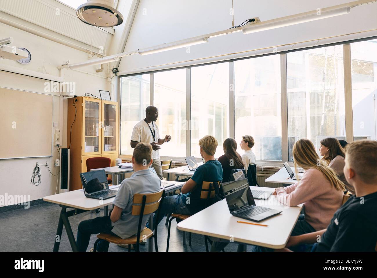 Professeur masculin enseignant des étudiants assis avec un ordinateur portable dans une salle de classe au collège Banque D'Images