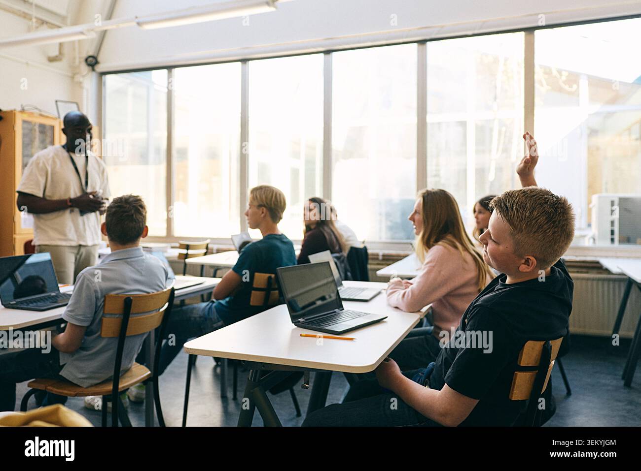 Étudiant masculin levant la main pendant la séance de questions et Réponses tout en étant assis en classe à l'école Banque D'Images