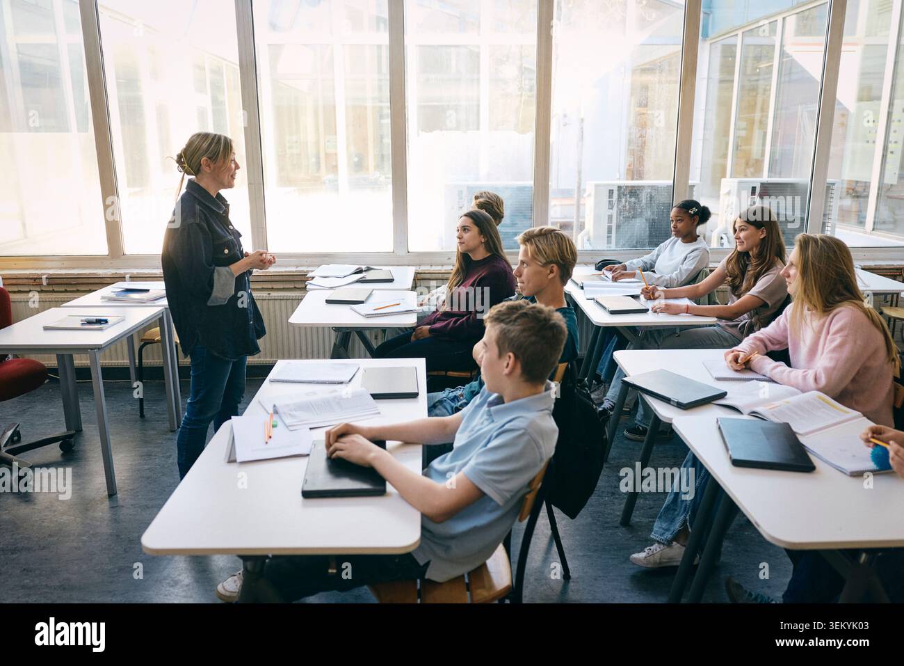 Professeure souriante parlant avec des élèves tout en enseignant en classe à l'école Banque D'Images