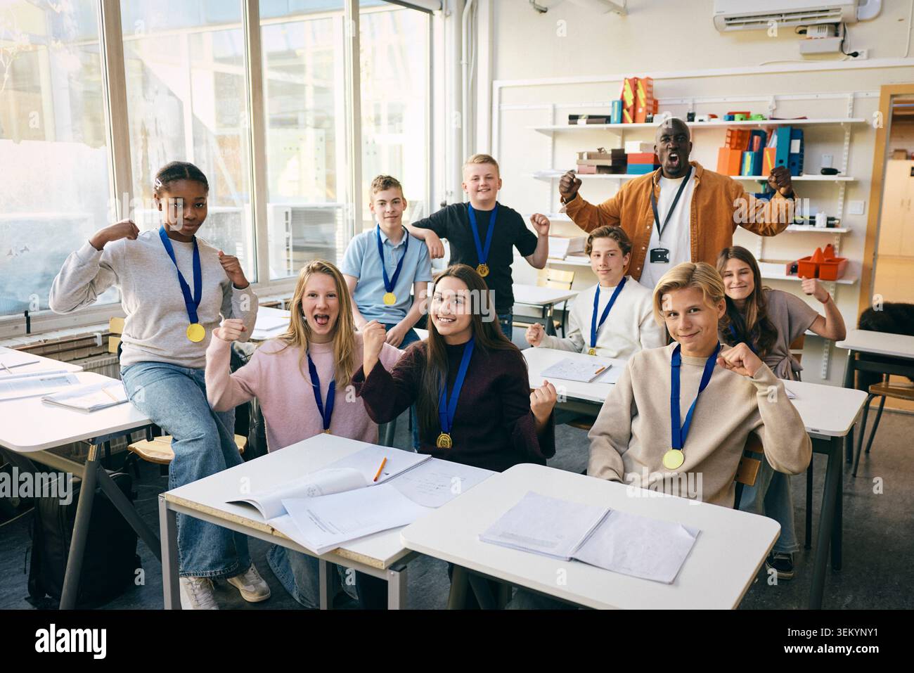 Portrait d'élèves du secondaire portant des médailles montrant le poing gagnant avec un professeur en classe à l'école Banque D'Images