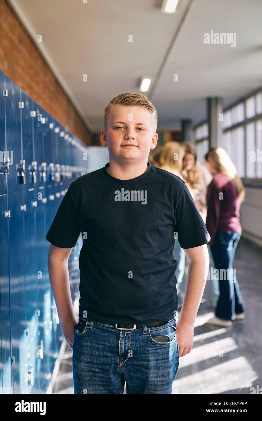 Portrait d'un garçon masculin junior élevé confiant debout près des casiers dans le hall de l'école Banque D'Images